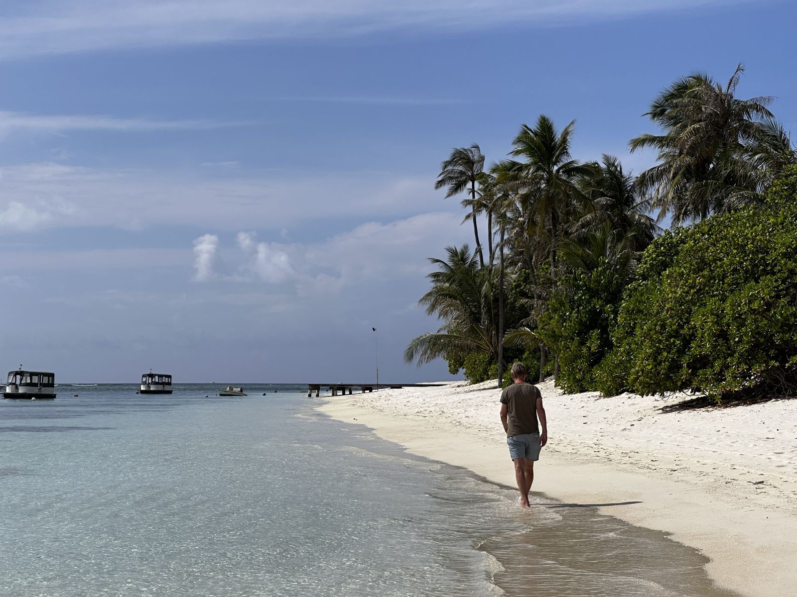 Kris wandelt langs het witte zandstrand en de palmbomen van Six Senses Kanuhura